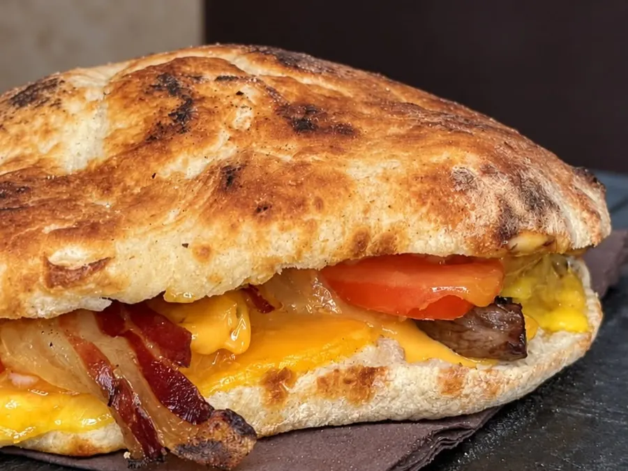 Un panino pizza farcito con bacon, formaggio fuso e pomodoro