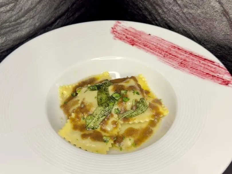 Ravioli in un piatto fondo bianco, con salsa ed erbe